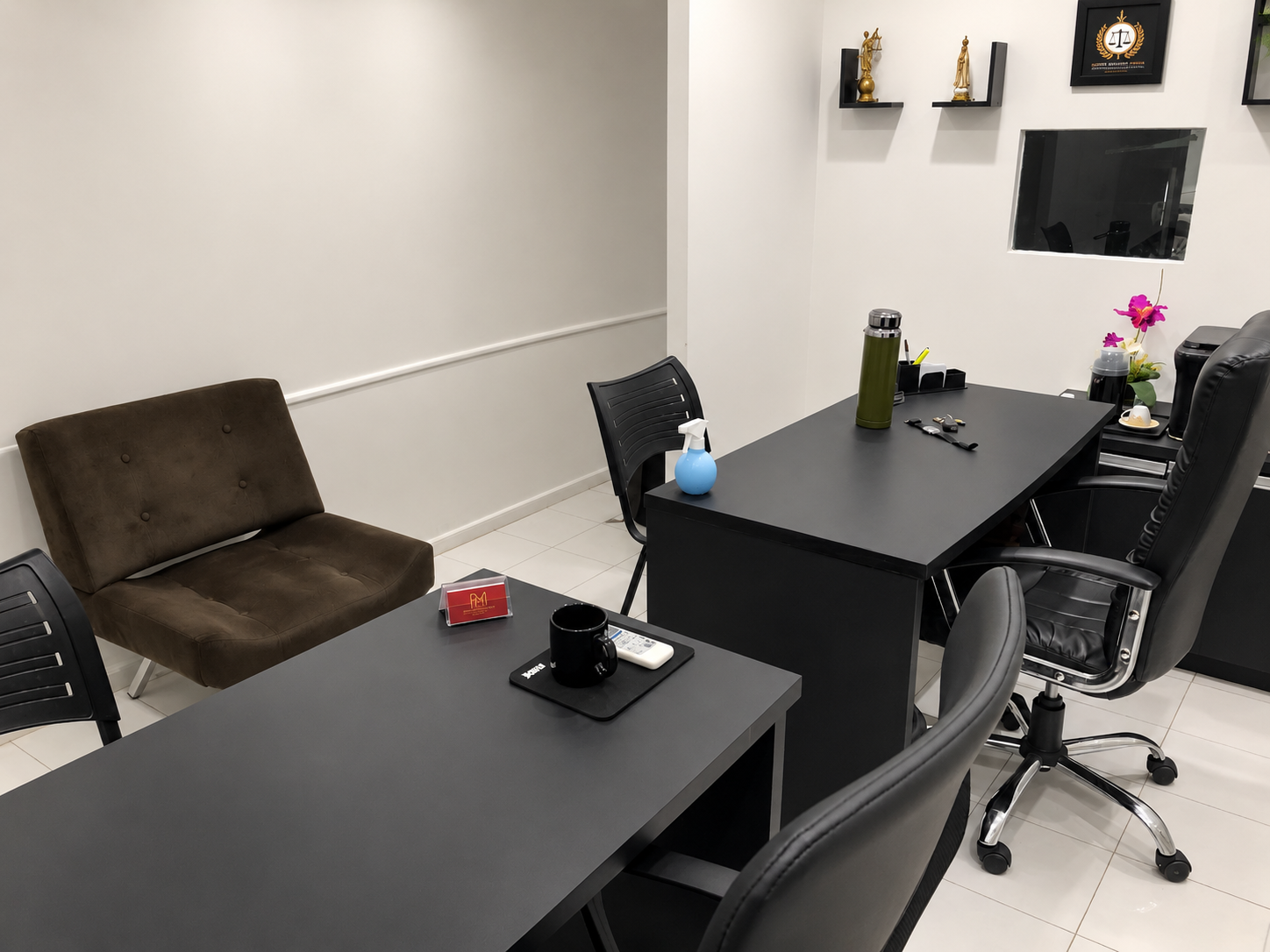 Interior do escritório com mesas pretas, cadeiras de atendimento e sofá junto à parede clara